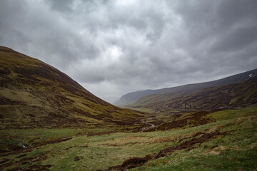 Majestic Scottish Highlands landscape with rolling hills and dramatic cloud formations near a remote valley