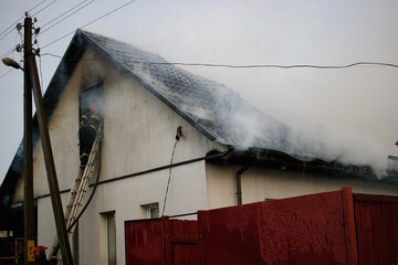 Flames engulf a roof as firefighters respond to the emergency in a residential area amidst thick...