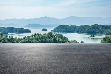 Gordijnen Asphalt road square and lake water with green mountain nature landscape under blue sky. Outdoor asphalt parking lot. © ABCDstock