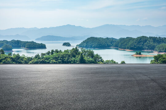 Asphalt road square and lake water with green mountain nature landscape under blue sky. Outdoor asphalt parking lot.