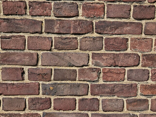 Closeup of a brown and red brick wall and the masonry between the rows of bricks.