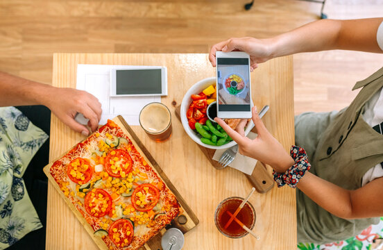 Top view of unrecognizable young girl taking video of fresh poke bowl salad with smartphone in a restaurant. Culinary blogger creating content for social media about healthy lifestyle and vegan food.