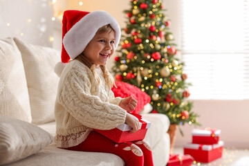Little girl in Santa hat sitting on sofa at home