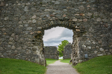 Obraz premium Explore the historic stone archway at castle ruins in Scotland surrounded by greenery and cloudy skies
