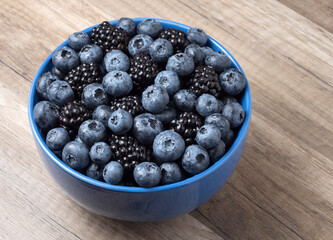 Bowl full of fresh blackberries and blueberries on a wooden background.