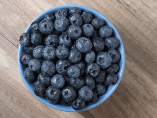 Bowl full of fresh ripe blueberries on a wooden background.