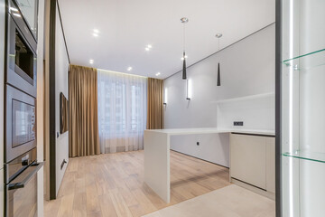 Laconic design of a modern studio apartment, decorated in white. A window with beautiful curtains, a kitchen set, a living room area with a TV.