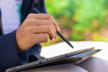 Close up of the hands of a digital artist using a digital pencil on a tablet, drawing outdoors in the open air.