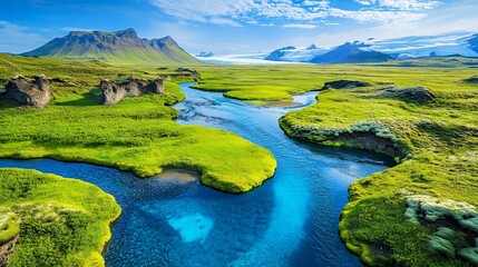 Naklejka premium Lush green valley with meandering river and glacier-capped mountains under a bright blue sky.