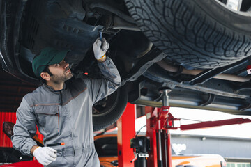 A skilled mechanic works under the vehicle and writes a detailed job checklist on a clipboard,...
