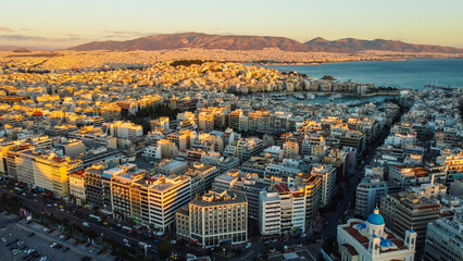 Visão aérea do pôr do sol sobre Atenas, Grécia, com luz dourada iluminando a cidade histórica e suas construções enquanto o céu se colore com tons alaranjados e rosas