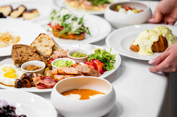 A beautifully styled breakfast spread featuring eggs, sausages, bacon, fresh vegetables, and toasted bread. Accompanied by creamy sauces and pastries, perfect for a delicious start to the day.