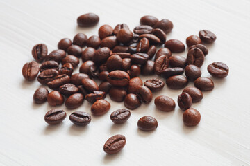 A pile of coffee beans on a white surface. The beans are of different sizes and shapes, and they...
