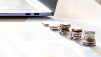 A pile of coins sits on top of a laptop. The coins are stacked in a pyramid shape, with the largest coin at the bottom and the smallest at the top. The laptop is open and placed on a table