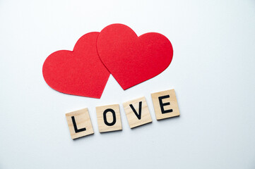 Word Love, composed with wooden squares, next to red hearts, on a white surface.