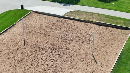 A side aerial view of a sand volleyball court with a net in a city park.