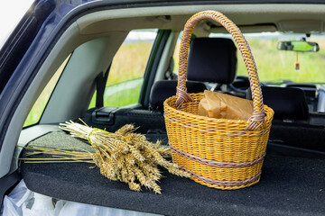 Woven basket with bread and wheat stalks resting in the trunk of a car near a field on a sunny day