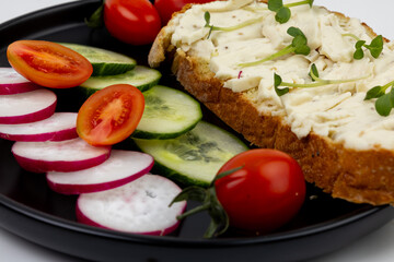 Fresh vegetable and soft cheese served on a black plate with sliced cucumbers, radishes, and cherry tomatoes at a casual dining setting