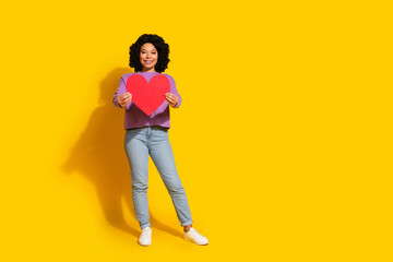 Fototapeta premium Full body portrait of pretty young girl paper heart empty space isolated on yellow color background