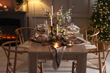 Christmas table setting with stylish dishware, glasses and burning candles in festive decorated room