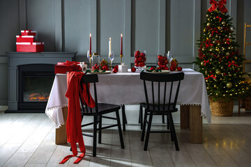 Christmas table setting with stylish dishware, glasses and burning candles in festive decorated room