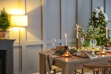 Christmas table setting with stylish dishware, glasses and burning candles in festive decorated room