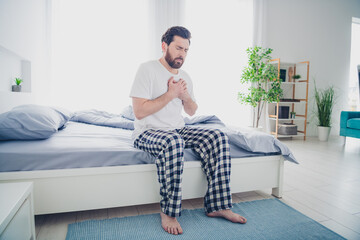 Photo of unhappy sad mature guy sleepwear pajama sitting bed having heart attack indoors home house...