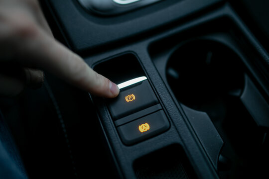 Car driver using fingers pushing electronic parking brake (EPB) in modern car for braking system