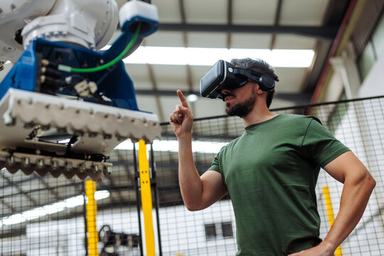 Industrial engineer wearing virtual reality headset controlling robotic arm in factory