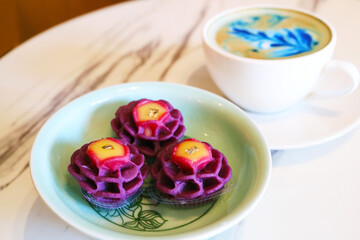 Artistic Flower Shaped Thai Dessert Made of Purple Sweet Potato and Mango Curd and a Cup of Cappuccino with Blue Latte Art