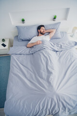 Top view vertical photo of cheerful positive young man dressed nightwear lying bed indoors house...