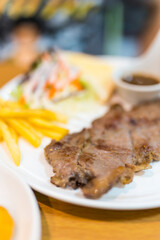 Delicious pork grilled steak served alongside French fries and a small salad on a white plate.