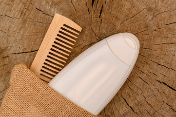 Wooden comb and white plastic shampoo container on wooden background.