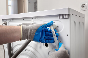 Plumber in gloves repairing washer on back side. Washing machine repair concept.