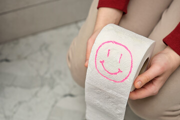 Woman sitting on toilet holding toilet paper with happy smiley face drawn. Conceptual funny image...