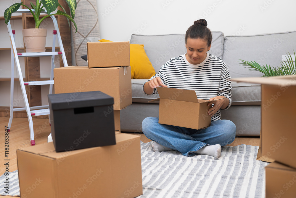Poster brunette lady with bun o head with delighted expression sits on sofa collecting cardboard boxes for 