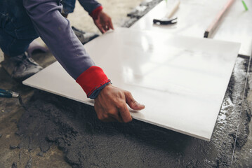 Worker hand laying ceramic tiles on adhesive glue cement floor at a construction site. Man work installs tile and building house.