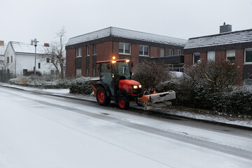 a tractor with a brush attachment removes snow from a road in a residential area after a snowfall. The concept is related to winter utility work and keeping roads clean.