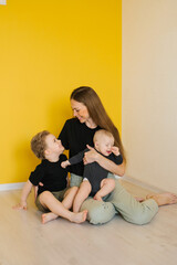 Young mother and her two children are sitting on the floor, with the mother holding the baby. Scene is warm and loving, as the family is spending quality time together