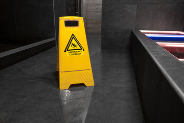 Warning sign Wet floor. Wet floor in the pool. Sauna. Bath. Moisture. Yellow color. Plastic sign. Gray floor. Tile. Yellow warning triangle on the floor with a black warning sign