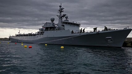 Naval ship docking amid cloudy skies at the harbor showcasing maritime operations and crew activities