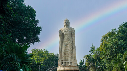 Majestic stone statue of a Buddha standing in an outdoor park with lush greenery and a serene...