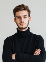 Fototapeta premium Young adult man in a black turtleneck sweater with arms crossed, studio portrait against a soft neutral background, showcasing confidence and style.