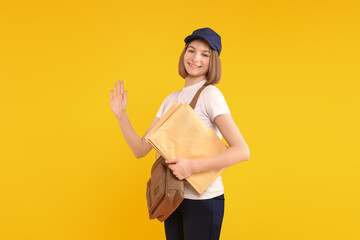 Happy postwoman with bag and envelopes waving hello on yellow background. Space for text