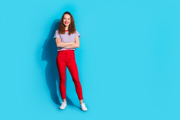 Confident young woman in vibrant red pants standing with arms crossed on a bright blue background