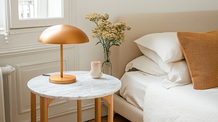 Close-up of a chic marble nightstand beside a bed, featuring a brass lamp and decorative white flowers, enhancing the bedroom's decor