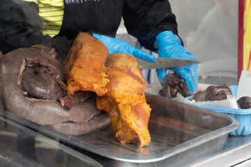 Blood sausage and marinated meat on a tray in the foreground as an unrecognizable person cuts blood sausage at a local food market. Preparation of fritanga, typical Colombian food.