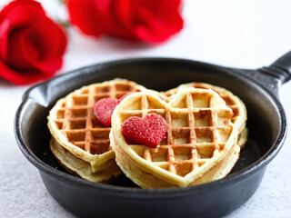 Heart-shaped waffles served in a skillet with romantic red roses in the background for a special breakfast occasion. Valentine&rsquo;s Day idea, date, engagement party, love party, eat, food