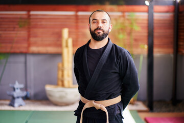 Portrait of a martial arts master posing in his dojo, wearing a black kimono and brown belt
