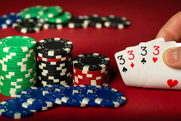 Player hand holding playing cards with winning combination four of a kind or quads on red poker table. Close-up of playing cards and different chips on table in club.